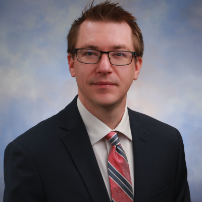 A man wearing glasses and a suit, smiling.